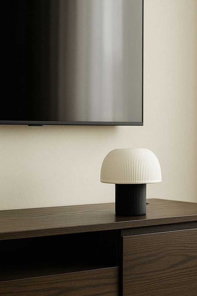 White textured table lamp on a wooden surface with a television in the background